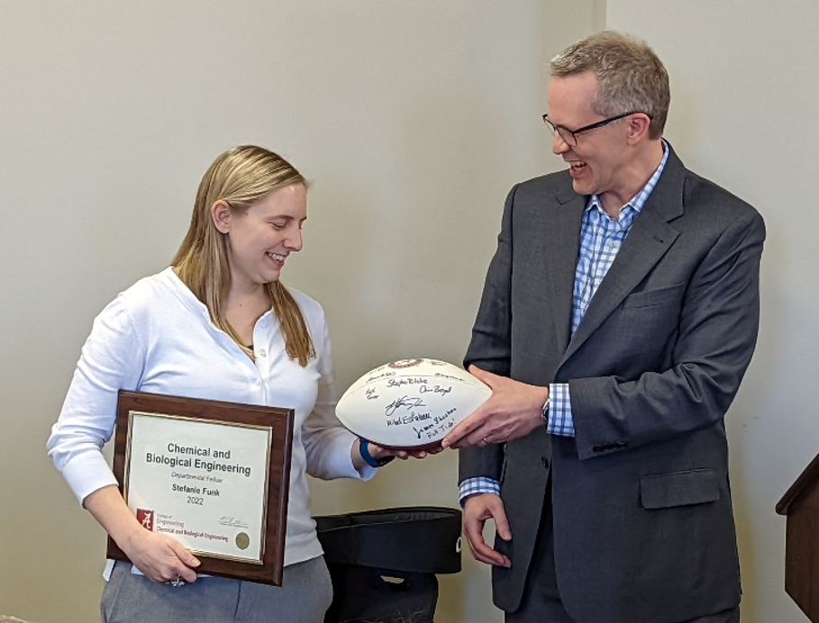 woman holding plack award is given a football by a man in a suit